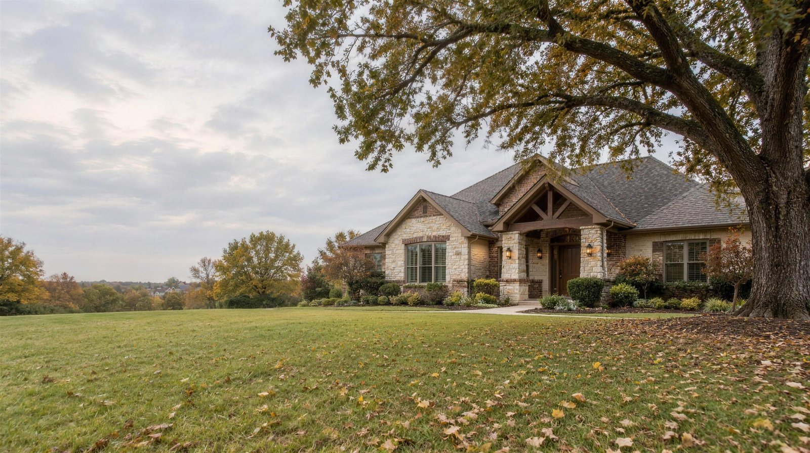Limestone and brick craftsman-style home beside a large pecan tree in Grapevine, Texas on an overcast autumn afternoon